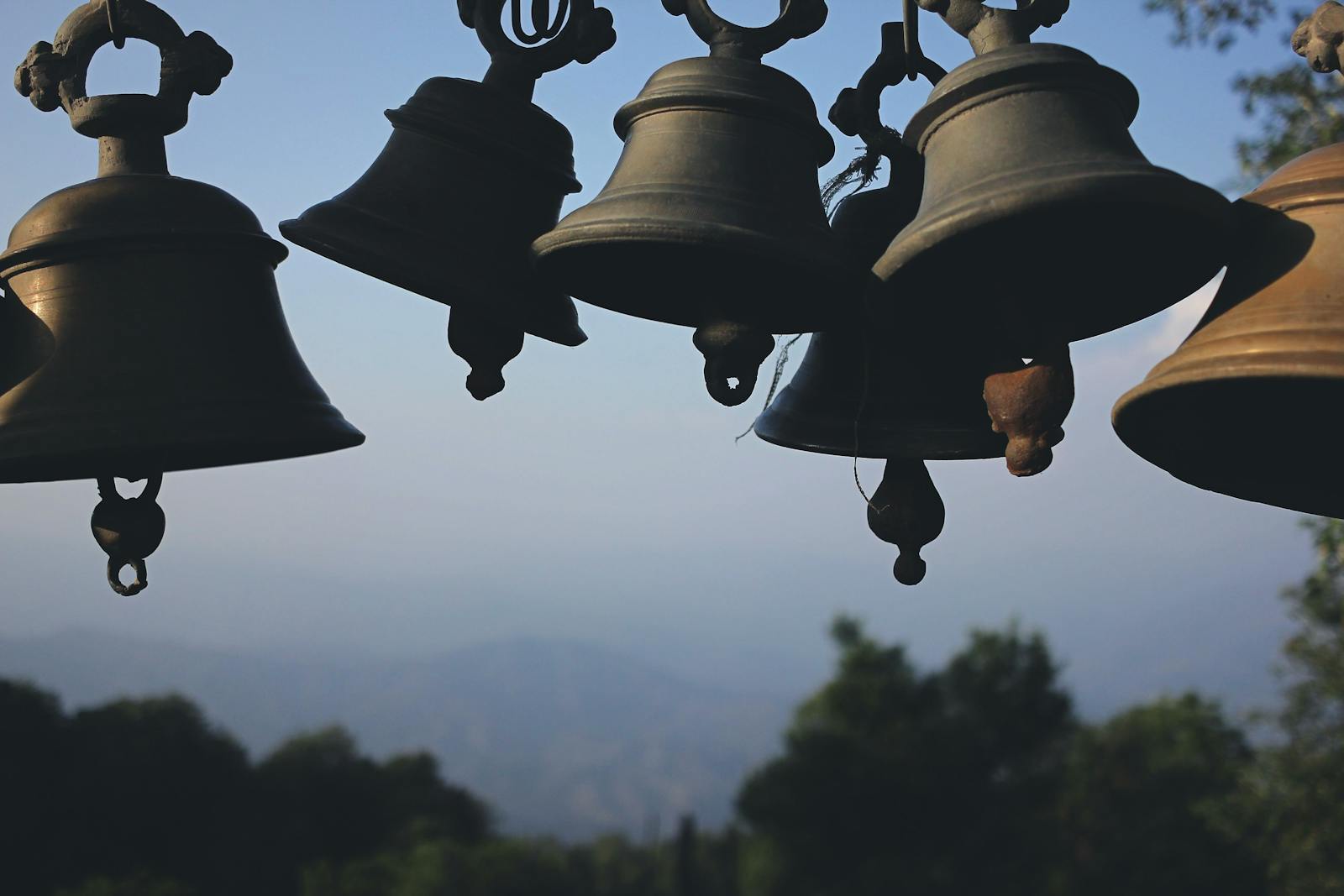 A collection of traditional hanging bells set against a scenic mountain backdrop, showcasing cultural heritage.