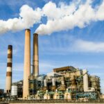 A large industrial power plant with smokestacks emitting smoke under a blue sky, symbolizing pollution.