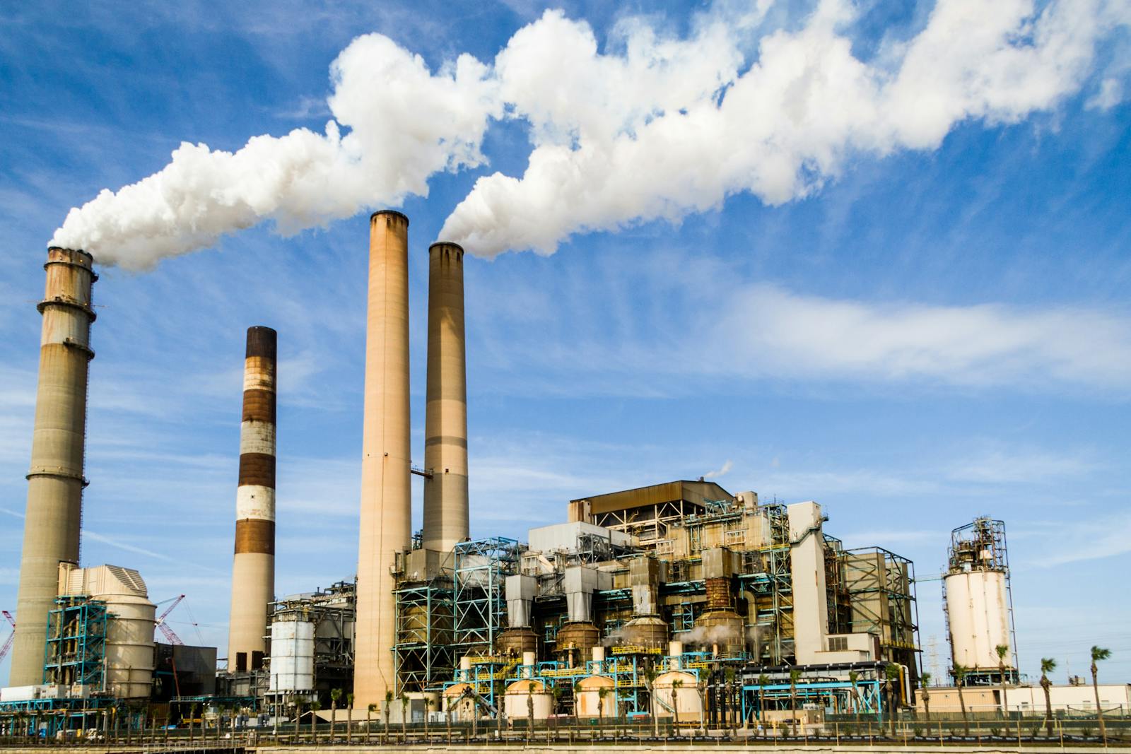 A large industrial power plant with smokestacks emitting smoke under a blue sky, symbolizing pollution.