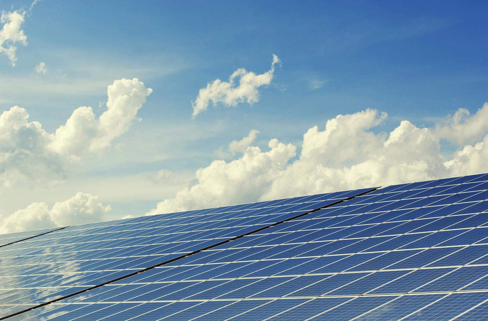 Sleek modern solar panels under a vibrant blue sky with clouds, symbolizing clean energy.