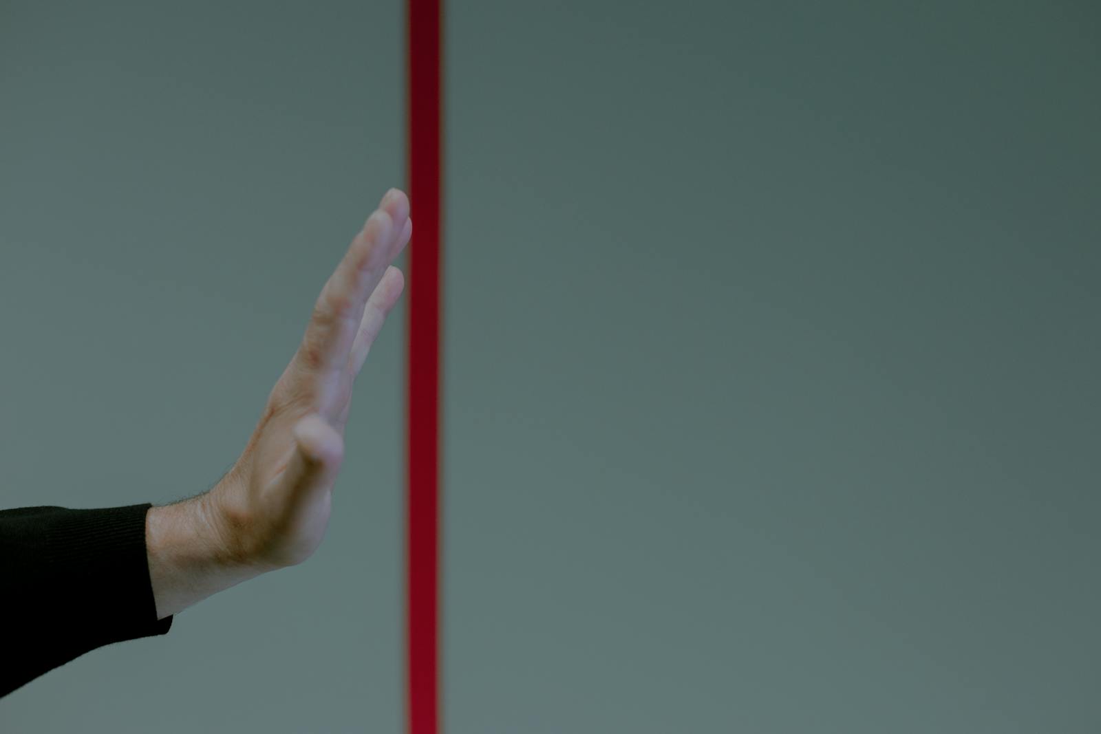 Close-up of a man's hand gesturing stop in front of a vertical red line, concept of boundary.