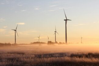 Wind turbines stand tall amidst a misty, sunrise landscape in Ontario, Canada, showcasing renewable energy.