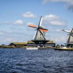 Scenic view of traditional Dutch windmills near water under a blue sky with clouds.
