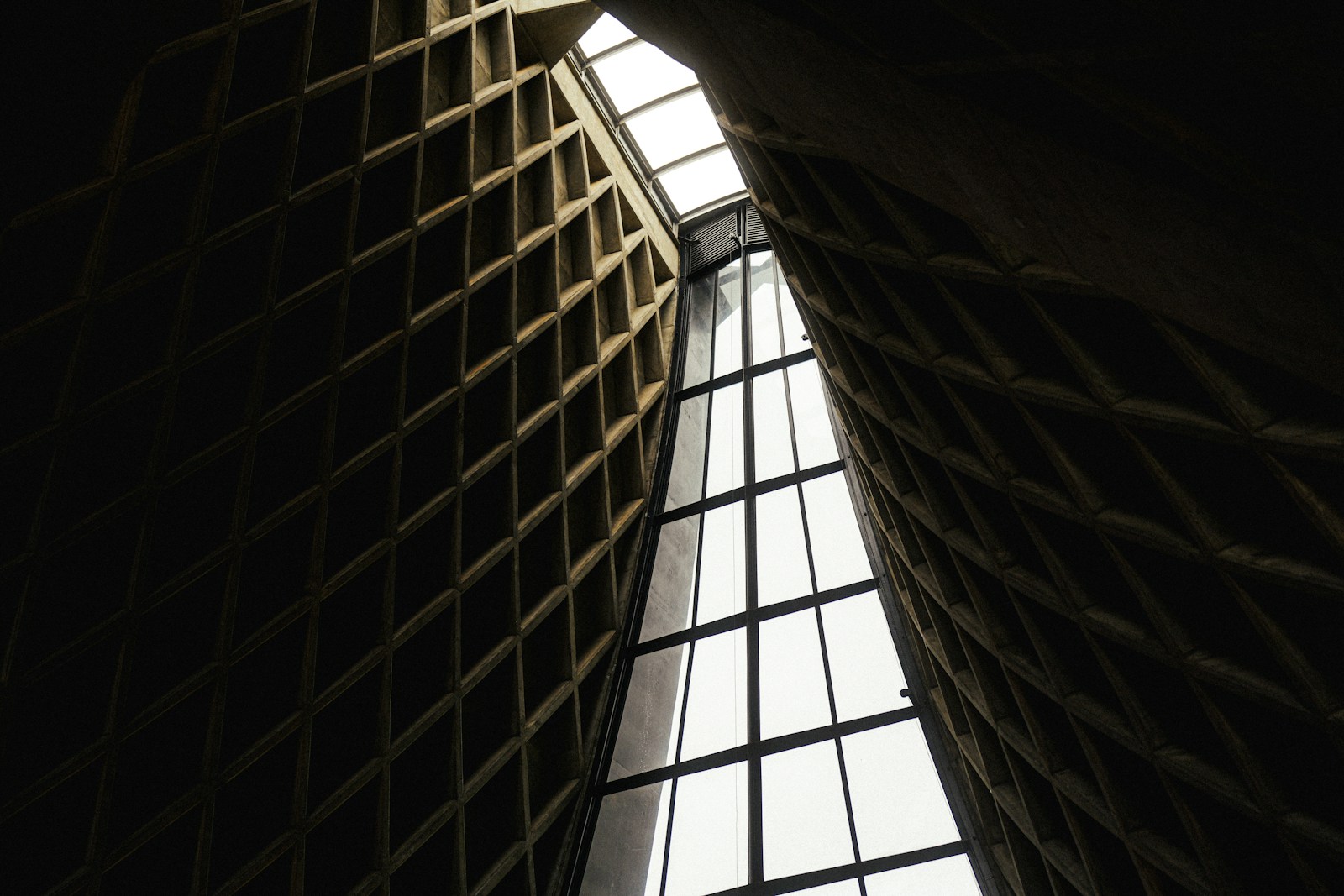 Dark, geometric architectural interior with bright central skylight.