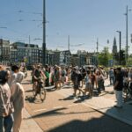 A crowd of people walking and cycling across a sunny intersection in Amsterdam