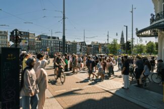 A crowd of people walking and cycling across a sunny intersection in Amsterdam