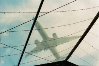 An airplane silhouette seen through a glass roof with dark structural beams and string lights